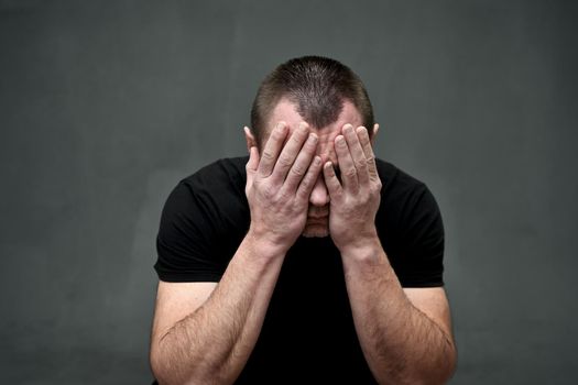 Portrait of a man closed his eyes with his hands in despair on a gray background