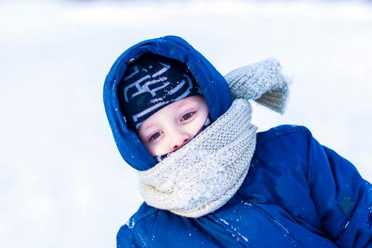 A smiling happy child lies in a snowdrift on a sunny winter day. A lot of snow and very frosty. Active winter outdoor games. The concept of a happy Christmas vacation.