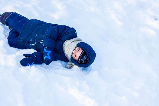 A smiling happy child lies in a snowdrift on a sunny winter day. A lot of snow and very frosty. Active winter outdoor games. The concept of a happy Christmas vacation.