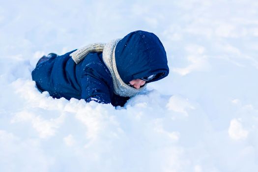 A smiling happy child lies in a snowdrift on a sunny winter day. A lot of snow and very frosty. Active winter outdoor games. The concept of a happy Christmas vacation.