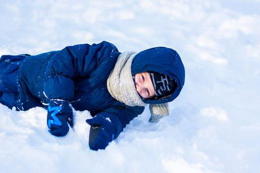 A smiling happy child lies in a snowdrift on a sunny winter day. A lot of snow and very frosty. Active winter outdoor games. The concept of a happy Christmas vacation.