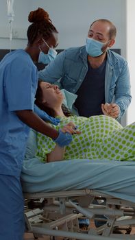 Screaming woman giving birth to child at maternity in hospital ward. Caucasian pregnant patient pushing while doctor and african american nurse helping with painful baby delivery