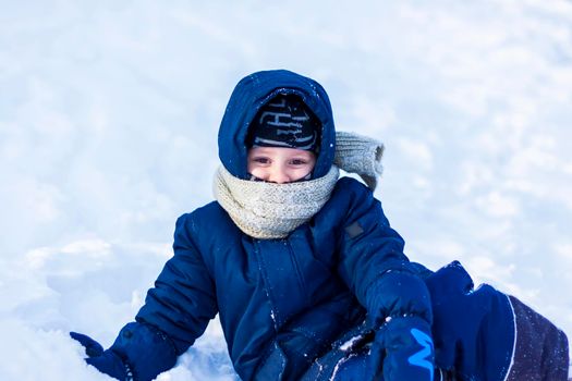 A smiling happy child lies in a snowdrift on a sunny winter day. A lot of snow and very frosty. Active winter outdoor games. The concept of a happy Christmas vacation.