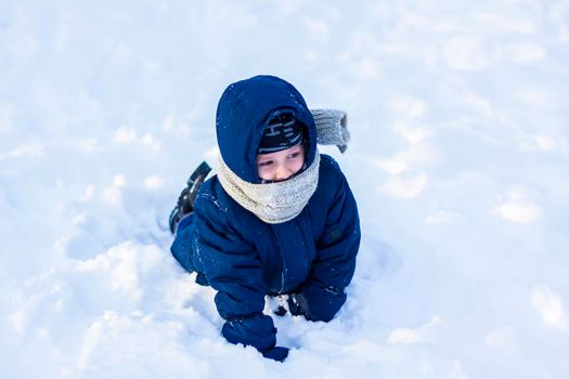 A smiling happy child lies in a snowdrift on a sunny winter day. A lot of snow and very frosty. Active winter outdoor games. The concept of a happy Christmas vacation.