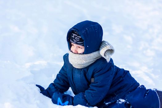 A smiling happy child lies in a snowdrift on a sunny winter day. A lot of snow and very frosty. Active winter outdoor games. The concept of a happy Christmas vacation.