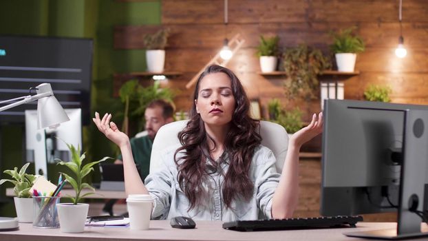Relaxed zen businesswoman with closed eyes standing in yoga position meditating during work pause in startup business company office. Entrepreneur worker concentrating on breathing