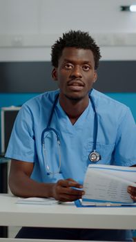 Man nurse talking on video call technology while sitting at desk in professional cabinet. Medical assistant using online remote communication and conference via internet for telemedicine