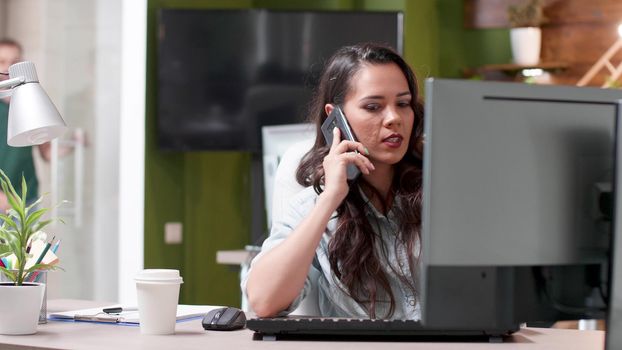 Executive manager sitting at table talking at modern smartphone with remote entrepreneur discussing management strategy. Successful businesswoman working at business presentation in startup office