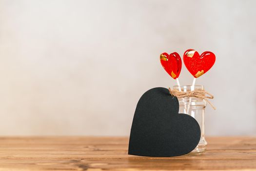 Still life Valentines day festive background with empty black chalkboard heart and 2 lollipop on wooden background. Mockup with copy space for design.