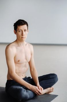 A male athlete with a bare torso is sitting in the gym before training and resting.
