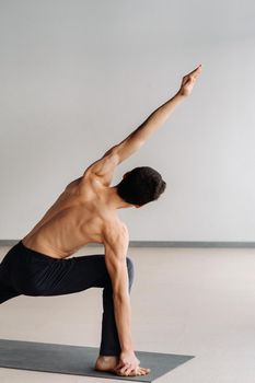 A man with a bare torso trains standing up, doing stretching in the gym.