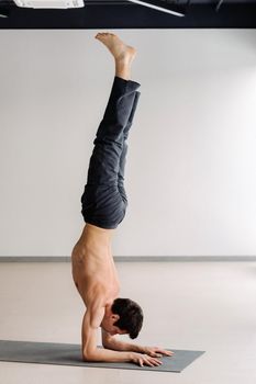 A man with a bony torso trains standing on his hands in the gym.