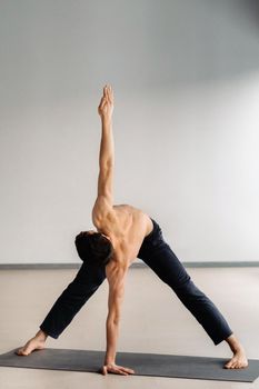 A man with a bare torso trains standing up, doing stretching in the gym.