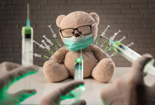 teddy bear in a medical mask with syringes in his shoulder on the doctor's table is given a second vaccination injection against the corona virus