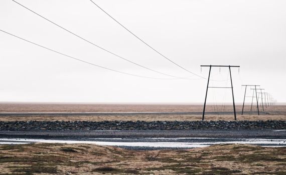 Power lines under white sky lost in the horizon of Iceland landscape