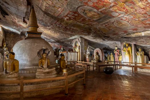 Sri Lanka. Dambulla Cave Temple. Buddha statues sitting in a row, illuminated by lamps from below, against the background of the stupa. High quality photo