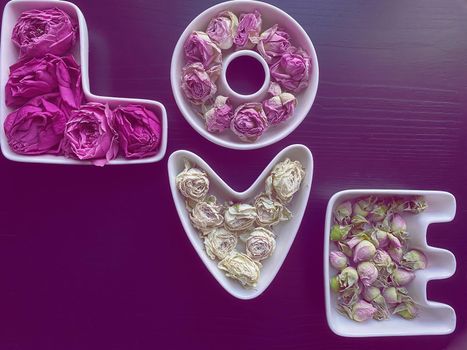 Valentine's day and love concept. The word love is made up of white porcelain molds filled with rosebuds on a dark wooden background. Purple toned image.