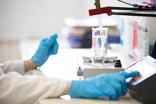The hands of a technician in blue rubber gloves are holding a flask. Pharmaceutical industry. Chemical laboratory