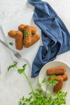 Meat croquets and parsley leaves on white ceramic dishes in a kitchen counter top.