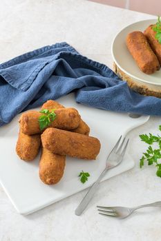 Meat croquets and parsley leaves on white ceramic dishes in a kitchen counter top.