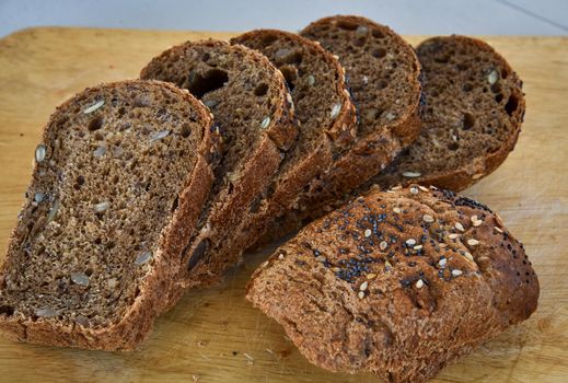 Sliced rye bread with sunflower and poppy seeds on rustic wooden background. Healthy food still life.