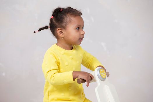 Little African American girl in a yellow dress with curly braids on a light background.
