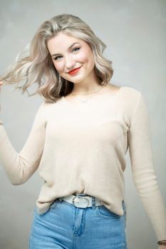 Beautiful young blonde girl in jeans and a beige sweater posing at the camera.