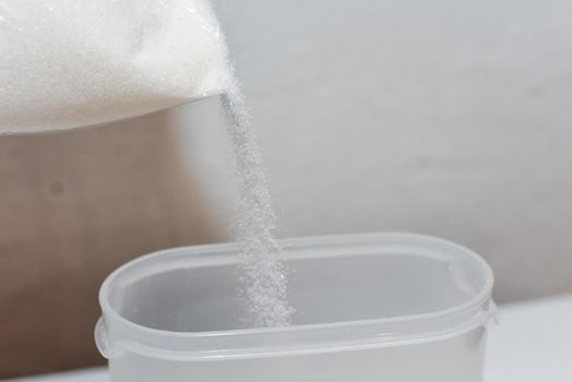 Storing sugar at home, arranging a place in the kitchen. Pouring sugar from a bag into a plastic container.