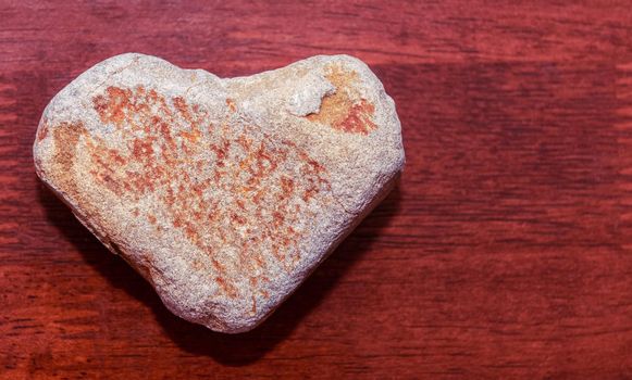 stone shaped like a heart on a wooden surface in red tone. Heart made of natural stone on a wooden background. Valentine's day and holiday concept.