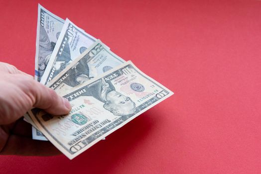 Mans hand hold dollar banknotes of different denominations Close up on red background.