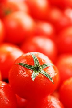 Ripe red tomatoes, with drops of dew. Close-up background with texture of red hearts with green tails. Fresh cherry tomatoes with green leaves. Group of juicy ripe fruit.