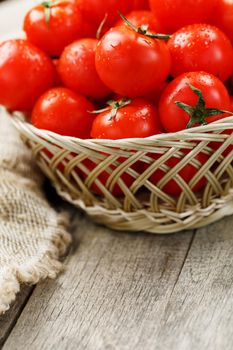 Small red tomatoes in a wicker basket on an old wooden table. Ripe and juicy cherry and burlap cloth, Terevan style country style Vertical frame