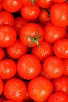 Fresh cherry tomatoes with green leaves. Background red tomatoes. A group of juicy ripe fruits.