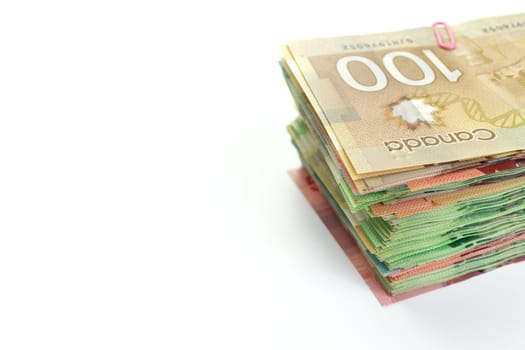 High Angle View of Large Stack of Canadian Banknotes on a White Background. Top bill is 100 one hundred and the bills below have values of 5 five, 10, ten, 20 twenty, and 50 fifty dollars. Copy Space on Left. High quality photo