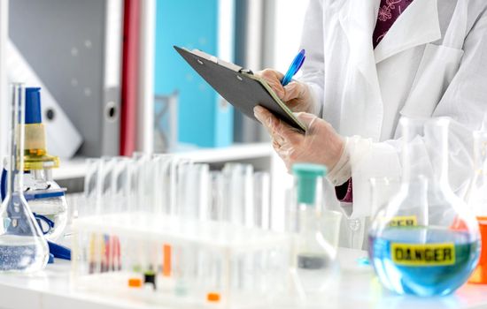 Girl during scientific chemistry experiment making notes close to table with tubes. Schoolgirl with chemical equipment on school lesson