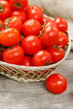 Small red tomatoes in a wicker basket on an old wooden table. Ripe and juicy cherry and burlap cloth, Terevan style country style Vertical frame