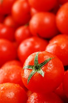 Fresh cherry tomatoes with green leaves. Background red tomatoes. A group of juicy ripe fruits.