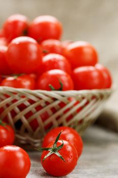 Ripe and juicy cherry tomatoes with drops of moisture in a wicker basket. Old wooden table, around the canvas of burlap. Country style.