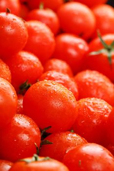 Fresh cherry tomatoes with green leaves. Background red tomatoes. A group of juicy ripe fruits.