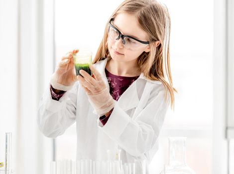 Girl doing scientific chemistry experiment wearing protection glasses. Schoolgirl with equipment and chemical liquids on school lesson