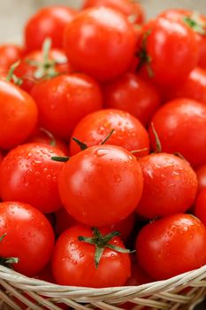 Small red tomatoes in a wicker basket on an old wooden table. Ripe and juicy cherry and burlap cloth, Terevan style country style Vertical frame