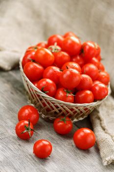 Small red tomatoes in a wicker basket on an old wooden table. Ripe and juicy cherry and burlap cloth, Terevan style country style Vertical frame