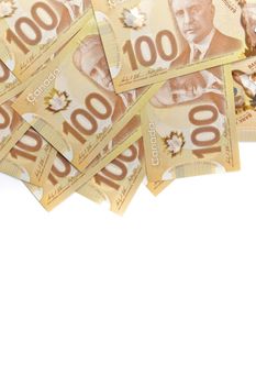 A Directly Above Image of Crisp Canadian 100 One Hundred Dollar Bills on a White Background. Banknotes are piled randomly on top of each other. Plenty of White Copy Space at bottom of frame. High quality photo