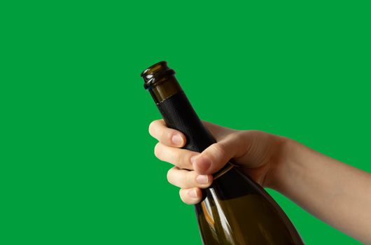 A woman's hand holding an open bottle of champagne on a green background.Holiday concept.