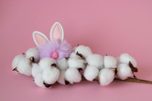 Beautiful white cotton flowers and a small fluffy lilac toy rabbit on a pink background. Easter Concept.