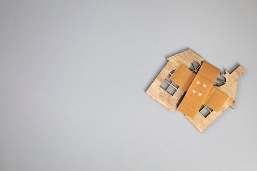 Closeup of broken house figure with crossed band aid on grey background top view, copy space, divorce, relationship problems, moving house, mortgage, space for text