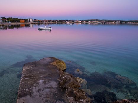 Dock, quay on island Vir, Croatia early in the morning. Dock and rubber boat overlooking beautiful purple and pink sky over Adriatic sea.