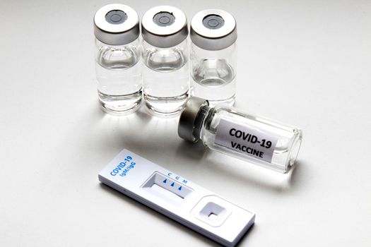 Rapid Antigen Diagnostic Test cassette of Coronavirus SARS-CoV-2 Covid-19 and vials with vaccine on white background