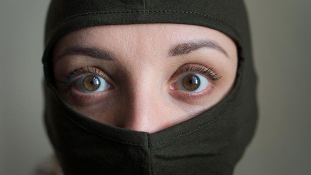 Female portrait of young girl wearing khaki balaclava, only eyes are visible, mandatory conscription, military, feminism, equality concept.