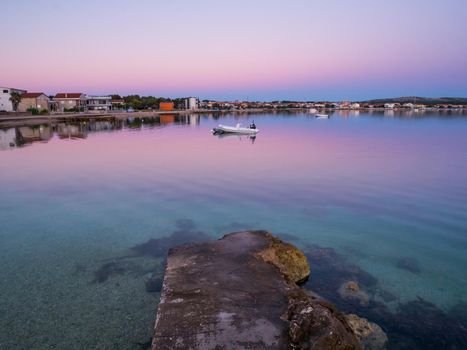 Dock, quay on island Vir, Croatia early in the morning. Dock and rubber boat overlooking beautiful purple and pink sky over Adriatic sea.